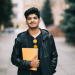 Handsome young indian student man read notebooks while standing on the street